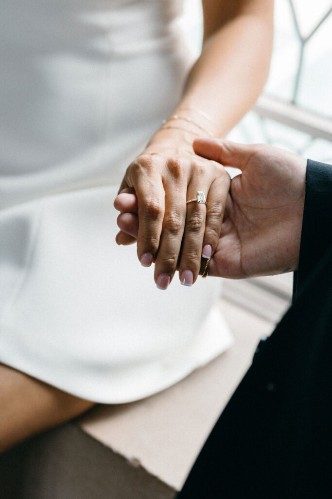 A close-up of a newlywed couple's hands holding each other at San Francisco City Hall, featuring a woman's hand with a diamond ring.